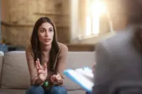A woman explains her mental health challenges to a therapist who sits across her taking notes