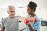a young nurse helping a senior patient to lift light dumbbells