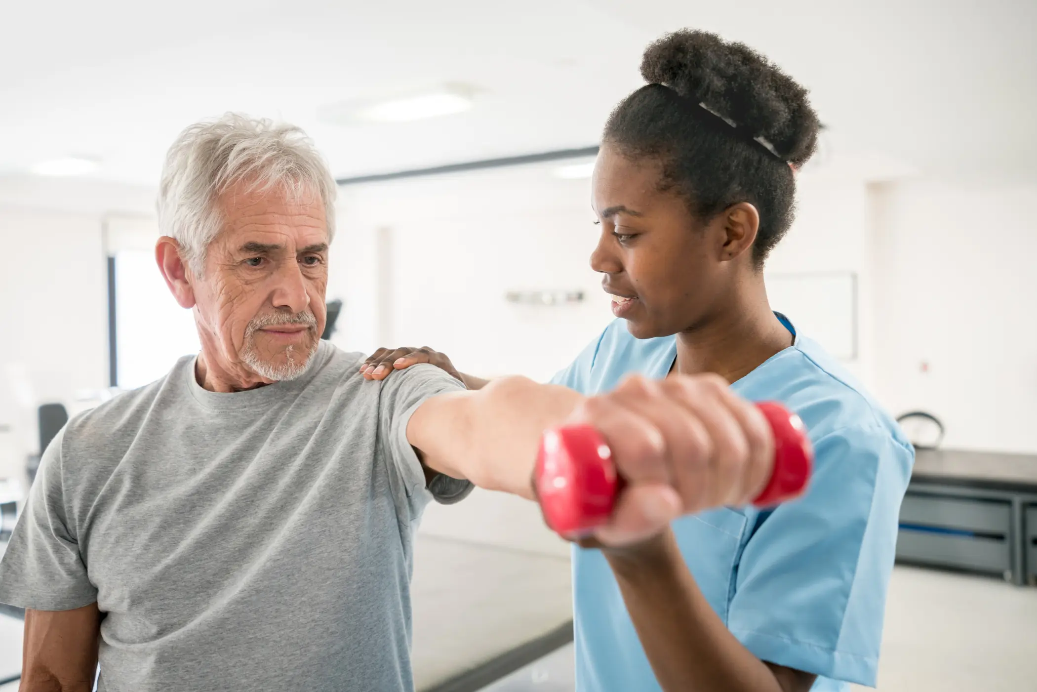 a young nurse helping a senior patient to lift light dumbbells